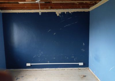 a bedroom renovation with bare ceilings and floors and newly painted dark blue walls
