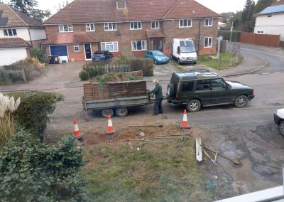 looking out of a bedroom window to a jeep loading a trailer with garden rubbish against a front garden area which is coned off with tools