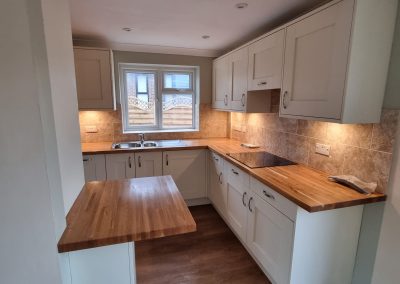 internal shot of a newly fitted kitchen with white units, dark wooden floors and wooden worktops looking out of a small window to wooden garden fence