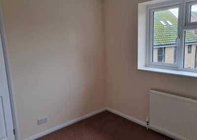 a newly painted bedroom with small window and light cream walls with a brown carpet and white paintwork