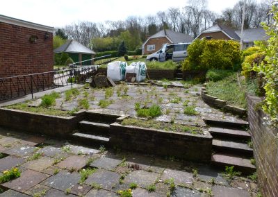 An old front garden area with paving surrounded entirely with weeds and 3 stepped up areas. Builders bags and van in background