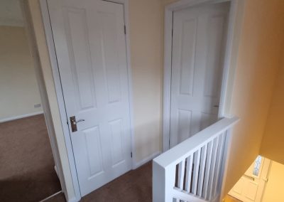a newly decorated landing area showing white handrail at top of staircase and two white doors into other rooms