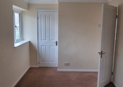 a newly painted small bedroom with 2 white doors, cream walls and mocha carpet