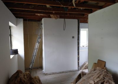 a stripped out room with bare ceilings and floors, piles of fibreglass and a ladder