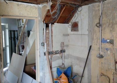 A newly fitted kitchen and hallway with white cupboards, built in oven, wooden worktops and wooden laminate flooring. Olive green paint on the walls.
