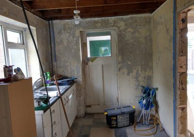 A stripped out kitchen during building works with builders toolbox, loose wires and dusty surround