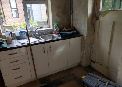 An old kitchen with stripped walls, old back door and sink area looking out over a window to another building