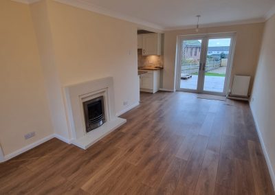 a newly decorated lounge diner with cream walls, new fireplace and white painted surrounds looking out of patio doors onto a patio and garden area
