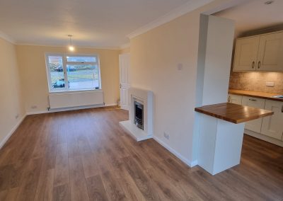 a newly refurbished lounge dining area with cream walls, white paint and wooden floor leading into side of kitchen area. No furniture in the room yet