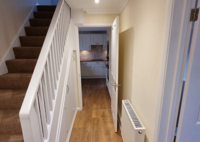 A newly decorated hallway with wooden laminate floor, white stair rails and cream painted walls