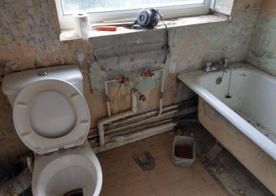 a before shot of an old bathroom with pipes, dirty toilet and bath in middle of renovation