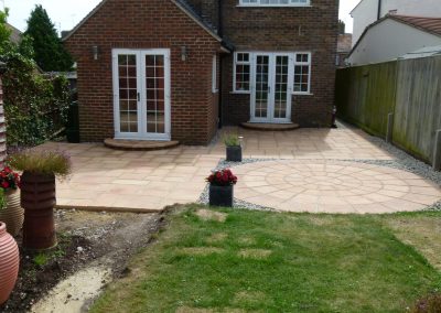a newly laid circular patio area with light coloured stones and gravel surrounds, looking towards a house