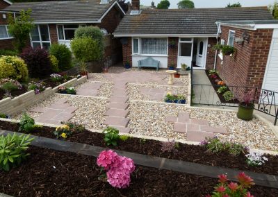 a newly laid front garden area looking down towards a bungalow. The garden has 3 stepped down areas with gravel and paving and planted areas surrounding