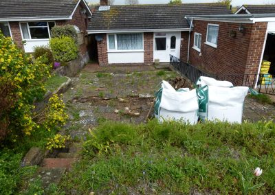 an old front garden with piles of builders bags and weeds