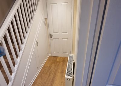 A newly decorated hallway with wooden laminate floor, white stair rails and cream painted walls