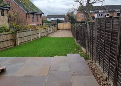 a newly landscaped back garden with new patio, middle section bright green lawn and far area in gravel with wooden fences surrounding