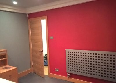 a bright red bedroom wall with a grey steel radiator and wooden bedroom door