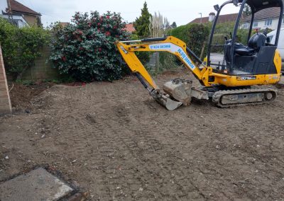a yellow digger on dug out front garden with rhodedendron bush at the side