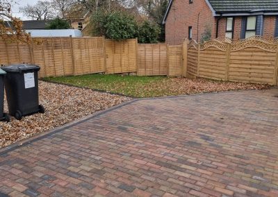 a new brick laid driveway area with gravel section to side, small lawn area and new light coloured wooden fencing