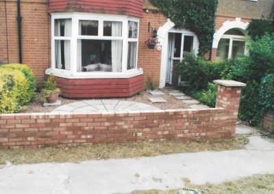 a semi detached house with white bay window and a new paved area and garden brick wall outside