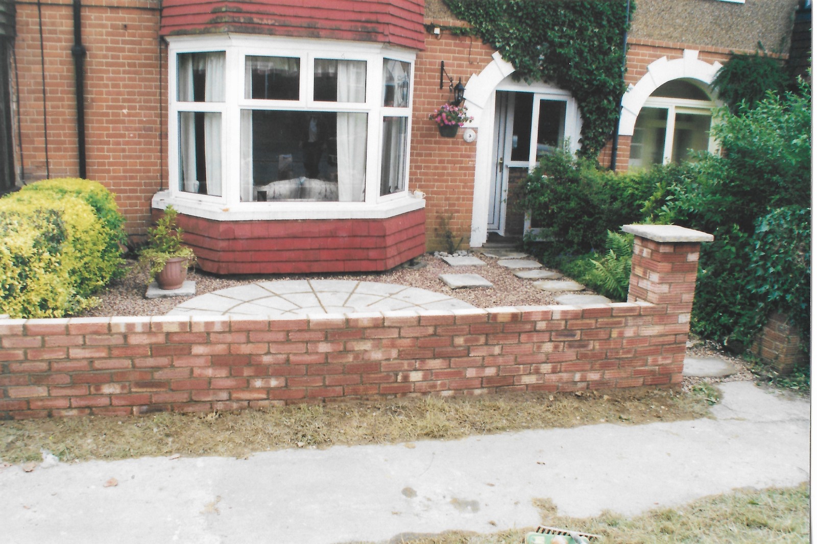 a semi detached house with white bay window and a new paved area and garden brick wall outside