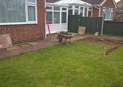 back garden project under construction - paving slabs lifted, marked out area with string and a wheelbarrow full of rubble.