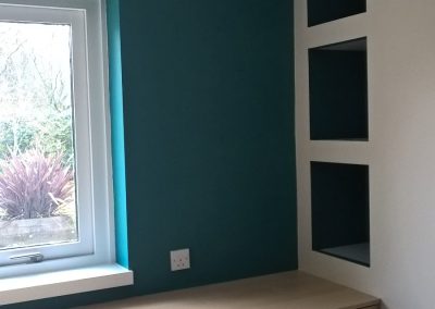 a small area of a bedroom with a turquoise wall next to a white wall with a window looking onto a garden