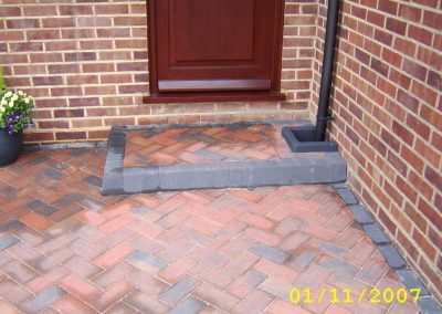 a new herringbone path and step in red brick with grey brick edging in front of a mahogany door