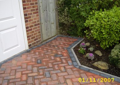 a new herringbone path in red brick with grey brick surround next to garden border with shrubs