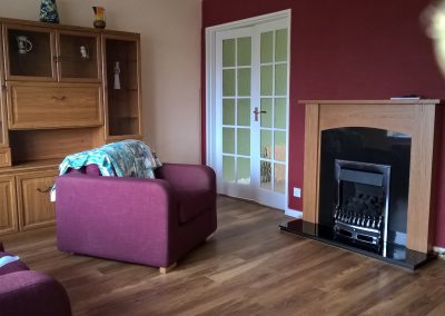 a living room area with white double doors, a new black fireplace, dark red walls, wooden floors and units and red armchairs
