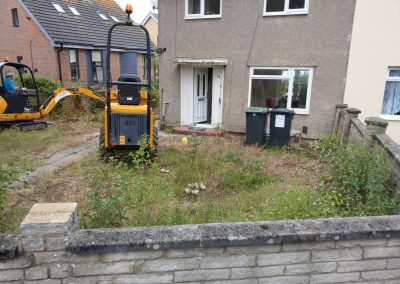 a grubby overgrown garden area with two diggers and lots of weeds and household wheely bins