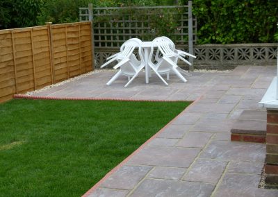 a small newly laid patio and lush green grass with white plastic dining set and new fence to the side