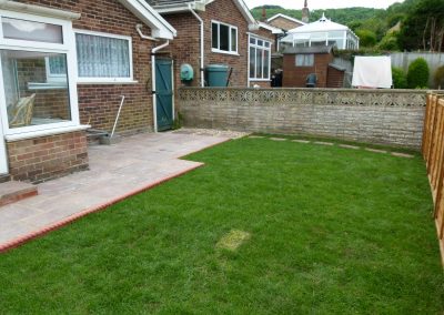 a small newly laid patio and lush green grass with a brick wall behind
