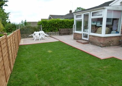 a small newly laid patio and lush green grass outside a conservatory with white plastic dining set and new fence to the side