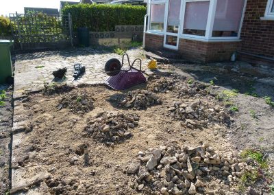 an old patio half dug up with upside down wheelbarrow, weeds and builders tools.
