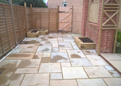 a new patio area with light slabs, against a light wooden fence on one side, a brick wall with light wooden trellis on the other side