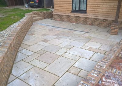 a new sandstone patio in light colours, with brick walls surrounding against a wooden clad house