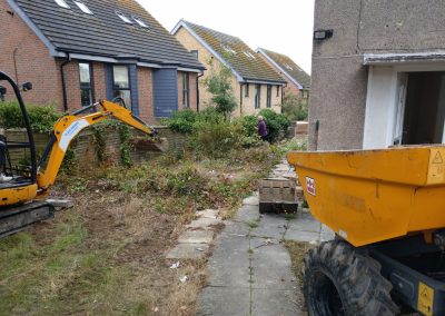 a building site of a garden with diggers and tools and huge areas of old paving and overgrowth