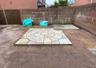 a new circular feature patio area with rubble surround and large red brick wall around the edge