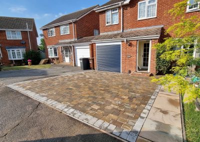 a detached house with blue garage door and newly laid brick driveway and garden path