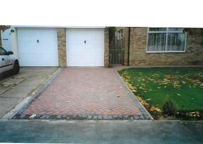 new red brick herringbone driveway with a white garage door and lawn to the right