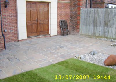 a newly laid patio in front of large wooden doors with new grass area and fence in background