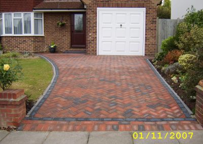 a new red and grey herringbone brick driveway in front of house with white garage door