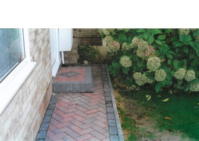 door step made out of red herringbone brick with grey brick edge against a grass area with hydrangea