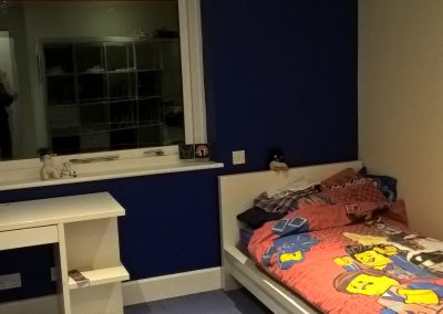 a small bedroom with single bed with childs duvet cover, a dark blue wall, white ceiling and light blue carpet