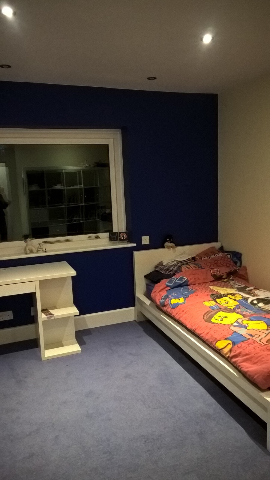 a small bedroom with single bed with childs duvet cover, a dark blue wall, white ceiling and light blue carpet