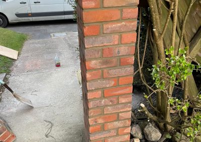 a newly built brick pier in red brick next to cut back hedge