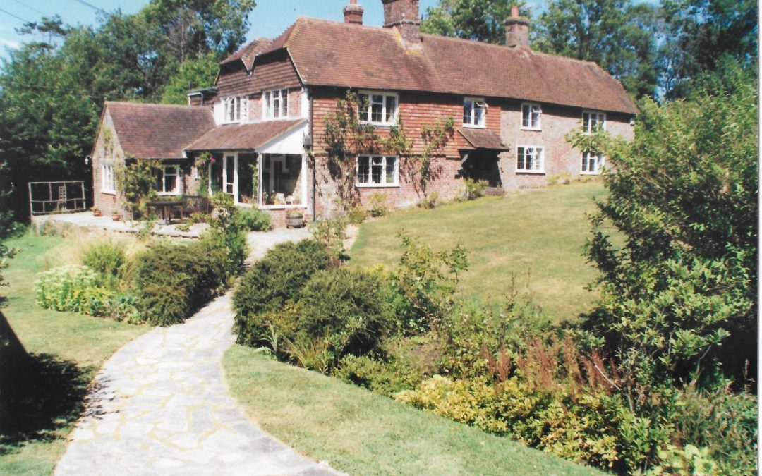 a beautiful large country house surrounded by green lawns and established garden beds with a newly laid paved path up to the door