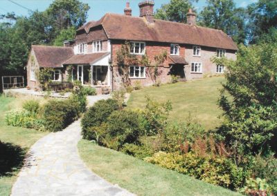 a beautiful large country house surrounded by green lawns and established garden beds with a newly laid paved path up to the door